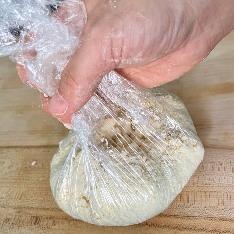 Image of Gather the corner and sides of the plastic and push the dough into the center and flatten to form a disk. This brings the dough together without overworking the mix or risking any melting from too much warm hand contact.